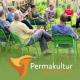 employees of the permaculture institute at a strategy meeting: you see people of different ages and genders sitting on green chairs in a circle on a fresh green meadow. a vegetable garden is indicated in the background and the people in the center of the picture are laughing